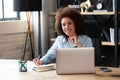 African American businesswoman smiles while working at laptop and making notes in her office Royalty Free Stock Photo