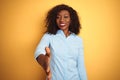 African american businesswoman wearing elegant shirt over isolated yellow background smiling friendly offering handshake as Royalty Free Stock Photo