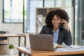 African-American businesswoman working on laptop at office using smartphone and financial graphs, Royalty Free Stock Photo