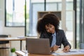 African-American businesswoman working on laptop at office using smartphone and financial graphs, Royalty Free Stock Photo