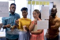 African american businesswoman writing strategy on glass wall amidst biracial colleagues at office Royalty Free Stock Photo