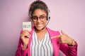 African american call center agent girl using headset holding reminder with help message with surprise face pointing finger to