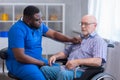 African-American caregiver and old disabled man in a wheelchair. Professional nurse and handicapped patient in a nursing