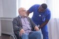 African-American caregiver and old disabled man in a wheelchair. Professional nurse and handicapped patient in a nursing