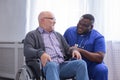 African-American caregiver and old disabled man in a wheelchair. Professional nurse and handicapped patient in a nursing