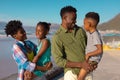 African american cheerful young parents carrying girl and boy while standing at beach against sky Royalty Free Stock Photo