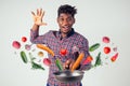 African american chef kitchener holding a frying pan wizard man cooking magic flying food salad, carrot, garlic, onion