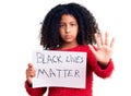 African american child with curly hair holding black lives matter banner with open hand doing stop sign with serious and confident