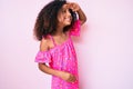 African american child with curly hair wearing casual dress very happy and smiling looking far away with hand over head Royalty Free Stock Photo