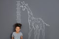 African-American child measuring height near chalk giraffe drawing