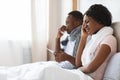African american couple sitting in bed, measuring fever, sneezing noses Royalty Free Stock Photo