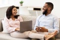 African american couple sitting on couch, using laptop and cellphone Royalty Free Stock Photo