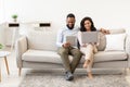 African american couple sitting on couch, using laptop and tablet Royalty Free Stock Photo