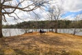 An African American couple sitting on a swing near a lake surrounded by lush green trees with blue sky and clouds