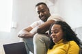 African american couple smiling and watching laptop and laughing at home. sitting on the sofa and the floor Royalty Free Stock Photo