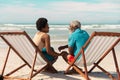 African american couple talking while sitting on deckchairs at sandy beach against cloudy sky