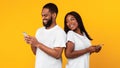 African american couple using smartphones, yellow studio wall Royalty Free Stock Photo