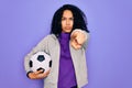 African american curly player woman playing soccer holding football bal over purple background pointing with finger to the camera Royalty Free Stock Photo