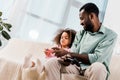 african american dad and daughter sitting on sofa and playing video game in Royalty Free Stock Photo