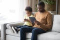 Black father and little son use gadgets sitting on couch