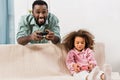 african american dad standing and playing video game with daughter in Royalty Free Stock Photo