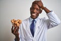 African american doctor man holding bowl with walnuts standing over  white background stressed with hand on head, shocked Royalty Free Stock Photo