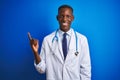 African american doctor man wearing stethoscope standing over isolated blue background with a big smile on face, pointing with Royalty Free Stock Photo