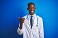 African american doctor man wearing stethoscope standing over isolated blue background smiling with happy face looking and Royalty Free Stock Photo
