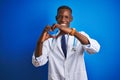 African american doctor man wearing stethoscope standing over isolated blue background smiling in love showing heart symbol and Royalty Free Stock Photo