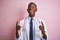 African american doctor man wearing stethoscope standing over isolated pink background amazed and surprised looking up and Royalty Free Stock Photo