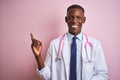 African american doctor man wearing stethoscope standing over isolated pink background with a big smile on face, pointing with Royalty Free Stock Photo