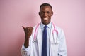 African american doctor man wearing stethoscope standing over isolated pink background smiling with happy face looking and Royalty Free Stock Photo