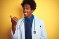 African american doctor man wearing stethoscope standing over isolated yellow background smiling with happy face looking and Royalty Free Stock Photo