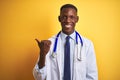 African american doctor man wearing stethoscope standing over  yellow background smiling with happy face looking and Royalty Free Stock Photo