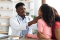 African american doctor palpating little girl throat at clinic