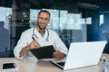 African american doctor portrait, man working inside modern clinic office at table using laptop, doctor in medical coat Royalty Free Stock Photo