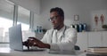 African-American american doctor wearing white coat typing on laptop in hospital office Royalty Free Stock Photo