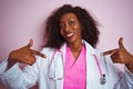 African american doctor woman wearing stethoscope over isolated pink background looking confident with smile on face, pointing Royalty Free Stock Photo