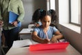 African american elementary schoolgirl writing on book at desk in classroom Royalty Free Stock Photo