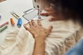 African-American employee sews cloth with machine tool at table in workshop