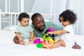 African-American family dad with kids babies play and collect a colorful pyramid at home on the bed, happy family