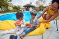 African american family outdoors by pool, mother with her two children, a boy and a girl eating watermelon fruit having fun Royalty Free Stock Photo