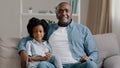 African american family sitting on sofa kid girl waving hello greeting adult father hugging daughter talking at camera Royalty Free Stock Photo