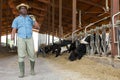 African american farmer holding agricultural tool and standing in cowshed