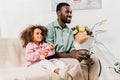 african american father and daughter sitting on sofa and playing video game together in Royalty Free Stock Photo
