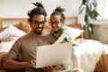 African american father with little son sitting in bedroom at home with laptop and watching cartoons