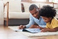 African American Father lying reading book on the floor with his son before traveling to work