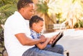 African American Father and Mixed Race Son Using Computer Tablet on Bench in Park Royalty Free Stock Photo