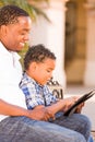 African American Father and Mixed Race Son Using Computer Tablet on Bench in Park Royalty Free Stock Photo