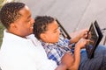 African American Father and Mixed Race Son Using Computer Tablet on Bench in Park Royalty Free Stock Photo